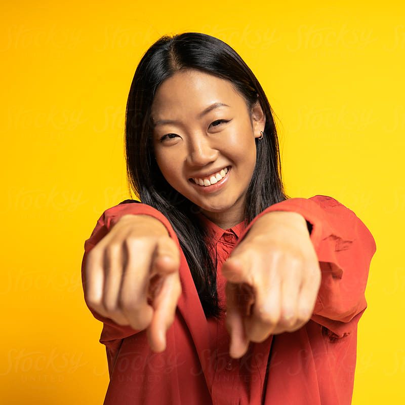 Portrait Of Happy Asian Woman Stock photo of attractive asian woman pointing with her fingers to the camera and smiling over yellow background in studio.